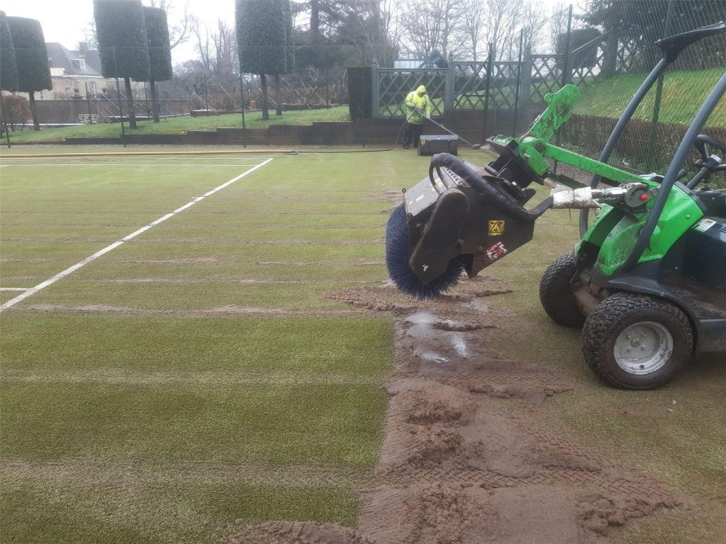 Machinery working on tennis court to get rid of thick moss and dirt on the surface