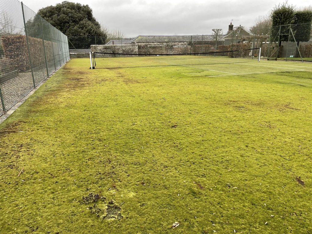 Tennis court in need of a deep clean with thick algae and moss build up on the surface